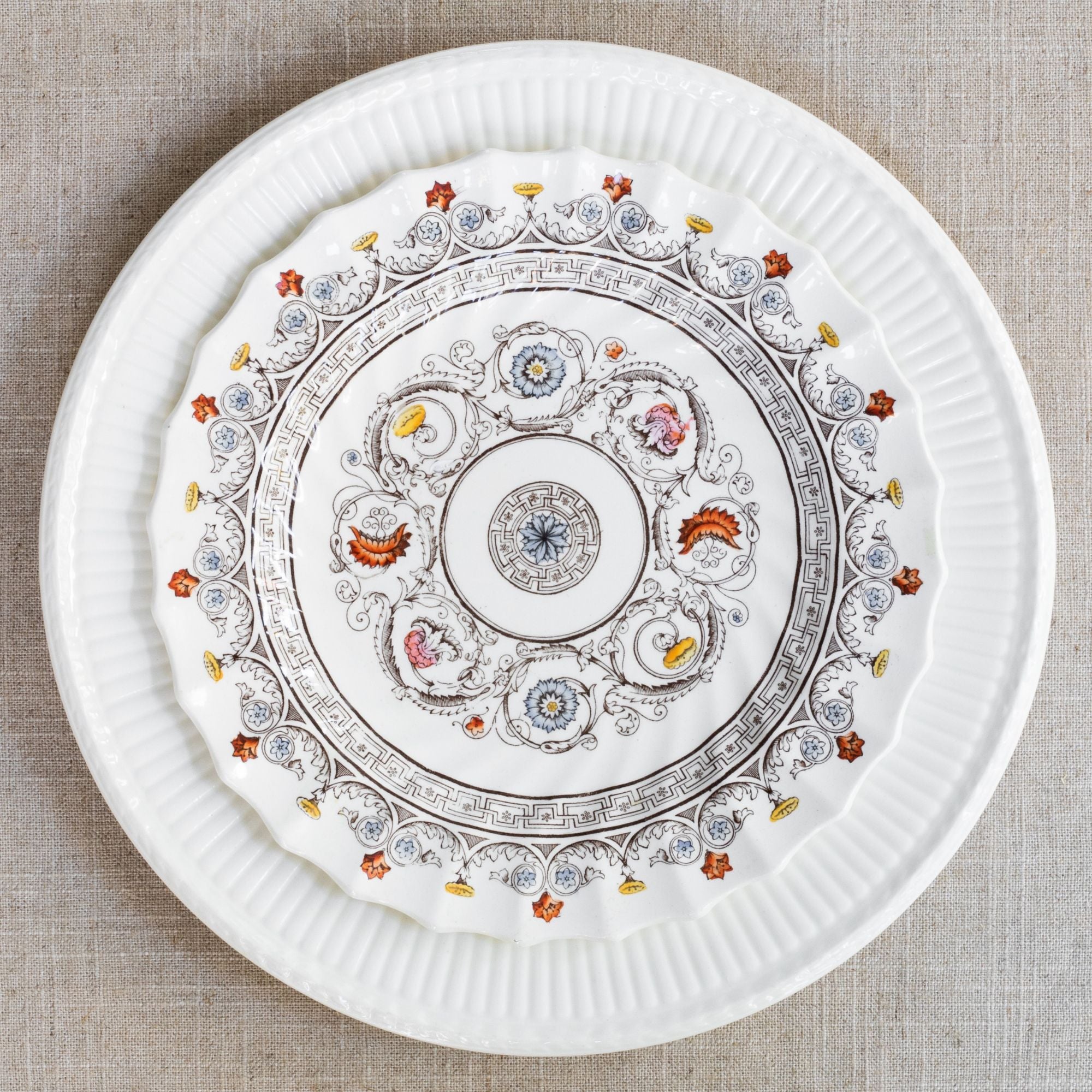 White ceramic charger plate topped with decorative plate featuring flowers and garlands around the edge and geometric center.