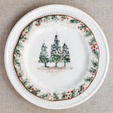 What ceramic charger plate topped with decorative salad plate featuring three Christmas trees and a holly and berry edge.
