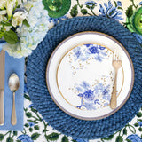 Greek pattern-edged charger plate topped with white salad plate with decorative blue flowers in Chinese art style and gold rimmed edges.