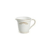 White ceramic creamer with gold floral design on a white background